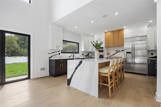 kitchen featuring light hardwood / wood-style floors, decorative backsplash, a kitchen island, white cabinetry, and stainless steel built in refrigerator