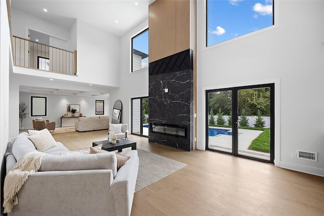 living room featuring a towering ceiling, a high end fireplace, and light wood-type flooring