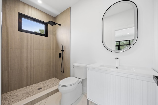 bathroom with tiled shower, a wealth of natural light, vanity, and toilet