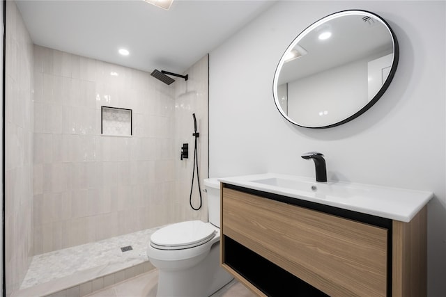 bathroom with toilet, tile patterned flooring, tiled shower, and vanity