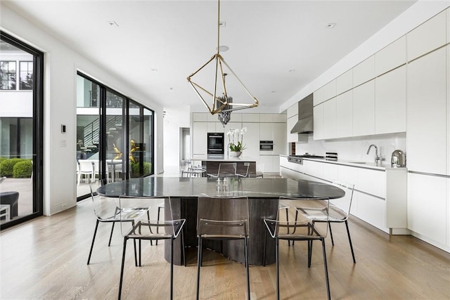 kitchen featuring wall chimney exhaust hood, pendant lighting, a large island, light wood-type flooring, and a kitchen breakfast bar