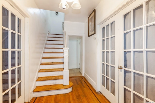 stairway featuring french doors, an inviting chandelier, and hardwood / wood-style floors