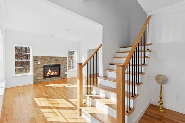 stairs featuring hardwood / wood-style floors, a stone fireplace, and ornamental molding