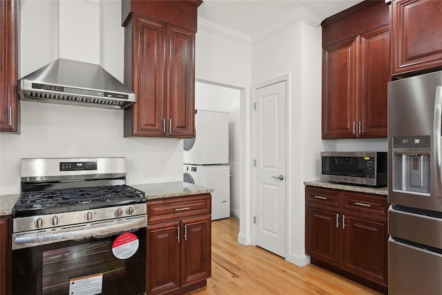 kitchen featuring crown molding, light stone countertops, wall chimney range hood, and appliances with stainless steel finishes