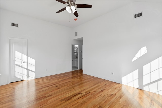 unfurnished room with light hardwood / wood-style floors, a towering ceiling, and ceiling fan