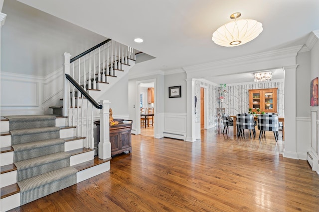 foyer with baseboard heating, hardwood / wood-style floors, ornamental molding, and a chandelier