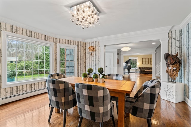 dining area featuring a notable chandelier, crown molding, hardwood / wood-style flooring, baseboard heating, and decorative columns