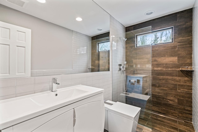 bathroom with tile walls, toilet, vanity, and a tile shower