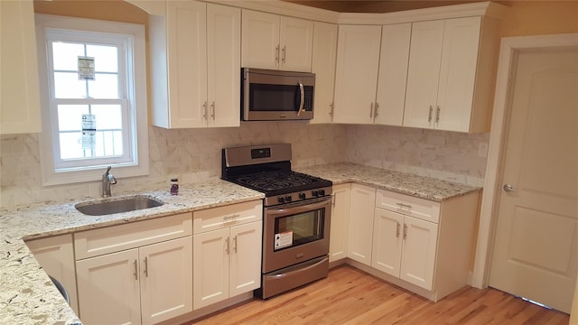 kitchen with stainless steel appliances, light stone countertops, white cabinets, and sink