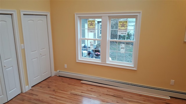 unfurnished bedroom featuring a baseboard heating unit and light hardwood / wood-style flooring