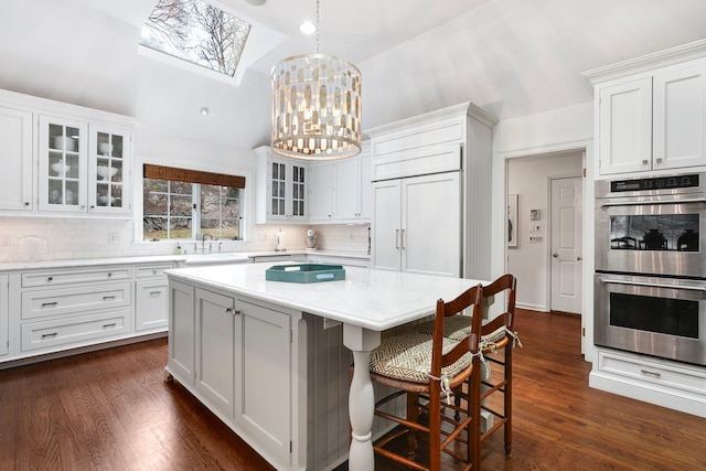 kitchen featuring white cabinetry, hanging light fixtures, double oven, and vaulted ceiling