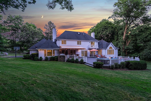 back house at dusk with a wooden deck, a yard, and a balcony