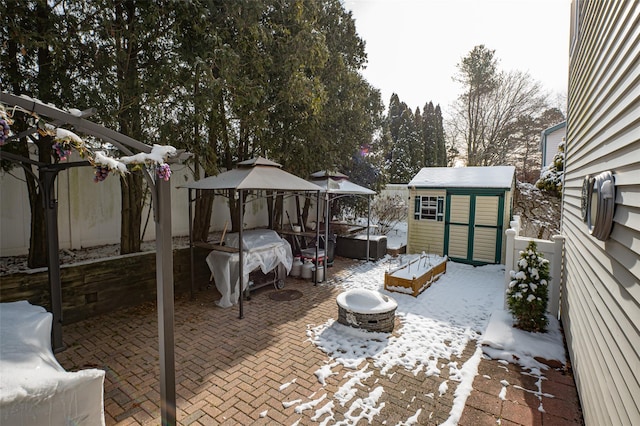 snow covered patio with an outdoor fire pit, a gazebo, and a storage unit