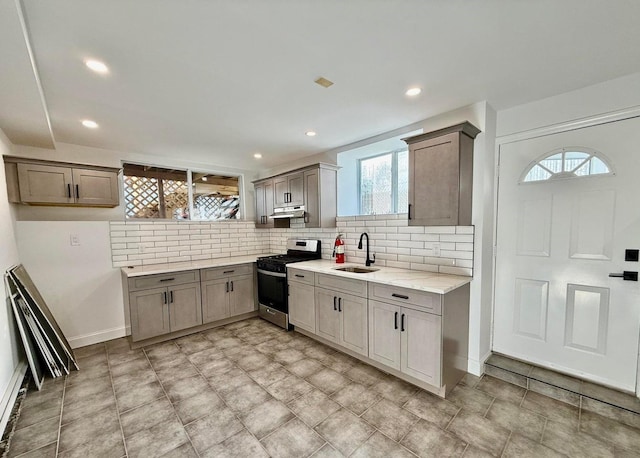 kitchen with gas stove, sink, tasteful backsplash, and light stone countertops