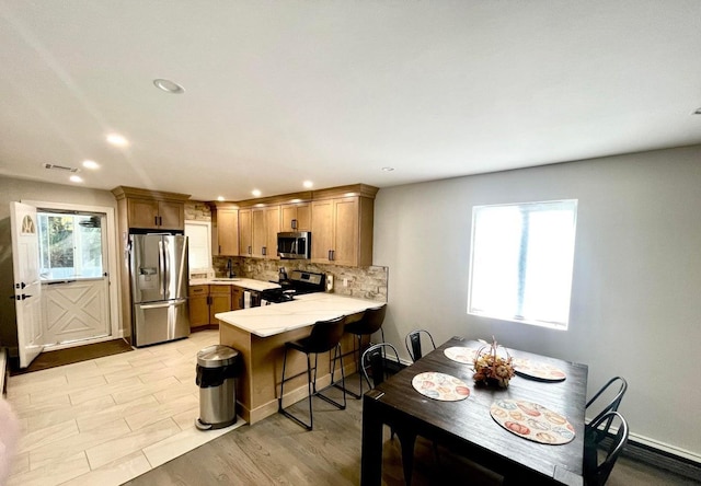 kitchen with sink, a kitchen bar, kitchen peninsula, decorative backsplash, and appliances with stainless steel finishes