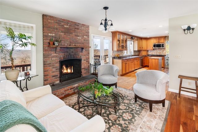 living room featuring hardwood / wood-style flooring, a chandelier, sink, and a brick fireplace