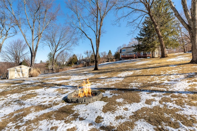 yard covered in snow with a storage unit and an outdoor fire pit