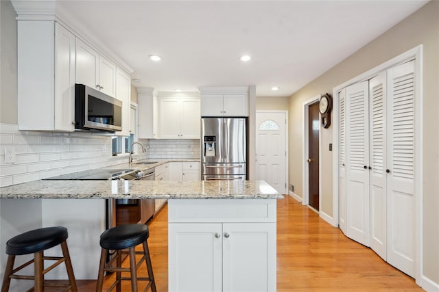 kitchen with light stone countertops, white cabinets, appliances with stainless steel finishes, decorative backsplash, and a kitchen breakfast bar