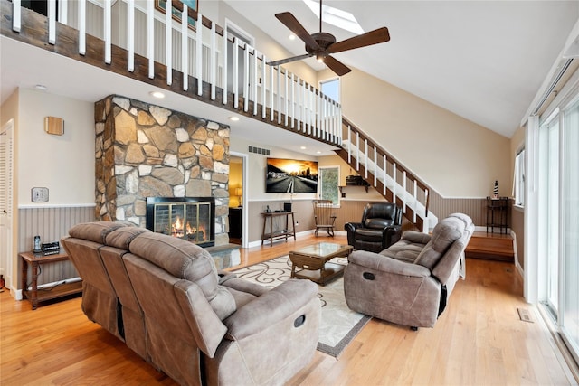 living room featuring high vaulted ceiling, a wealth of natural light, a stone fireplace, and light hardwood / wood-style flooring