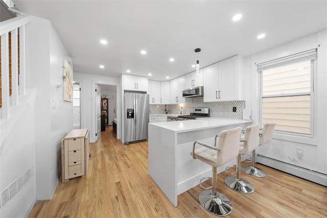 kitchen with white cabinetry, stainless steel appliances, light hardwood / wood-style floors, hanging light fixtures, and kitchen peninsula