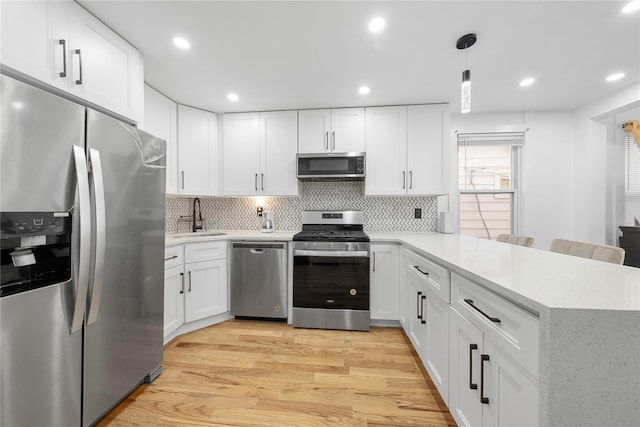 kitchen with hanging light fixtures, kitchen peninsula, stainless steel appliances, and white cabinetry