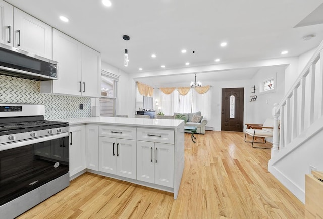 kitchen with decorative light fixtures, white cabinetry, stainless steel appliances, decorative backsplash, and light hardwood / wood-style floors