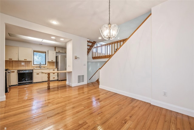 unfurnished living room featuring sink, a chandelier, and light wood-type flooring