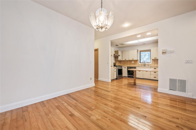 unfurnished living room with sink, a notable chandelier, and light hardwood / wood-style floors