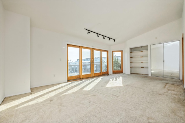 unfurnished bedroom with lofted ceiling, light colored carpet, rail lighting, and french doors