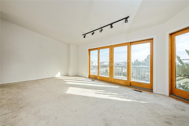 unfurnished living room with french doors, a wealth of natural light, rail lighting, and carpet flooring