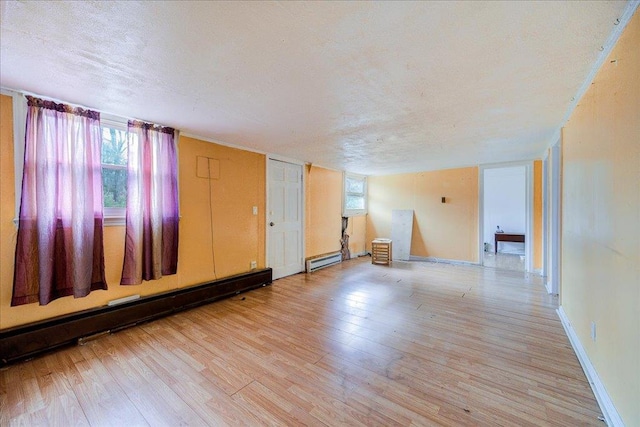 empty room with light wood-type flooring, a textured ceiling, and a baseboard radiator