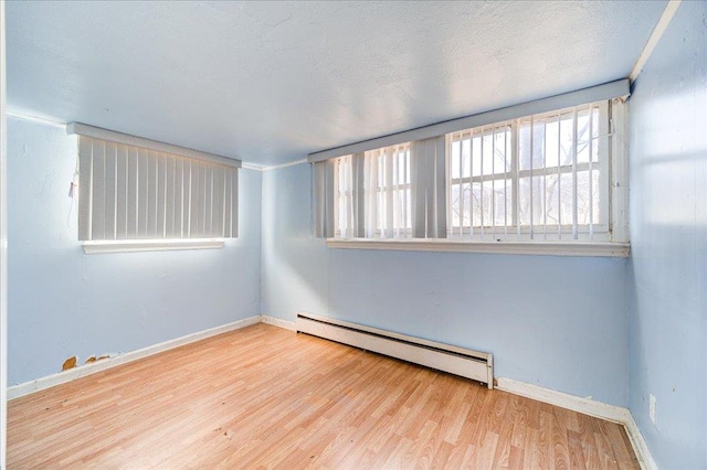 empty room with a textured ceiling, plenty of natural light, light hardwood / wood-style floors, and a baseboard radiator