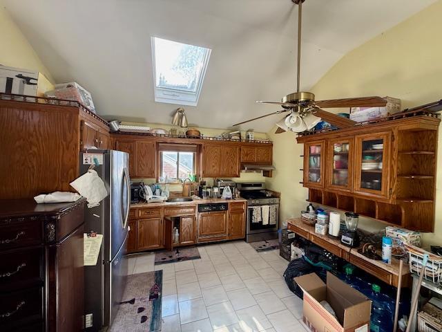 kitchen with ceiling fan, vaulted ceiling with skylight, sink, appliances with stainless steel finishes, and light tile patterned floors