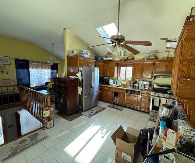 kitchen featuring vaulted ceiling with skylight, stainless steel appliances, sink, ceiling fan, and light tile patterned floors