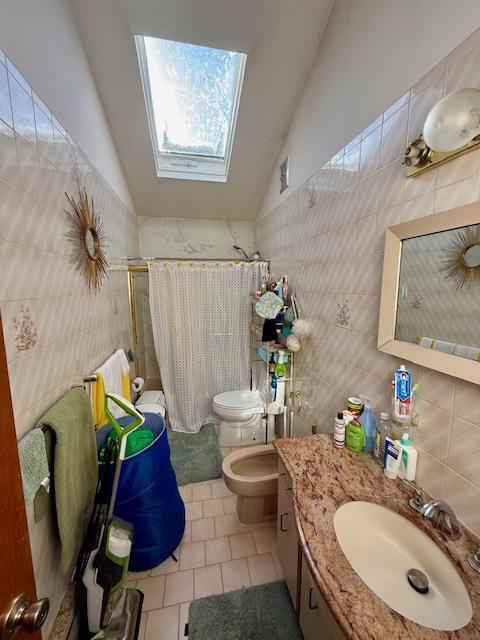 bathroom featuring toilet, vaulted ceiling with skylight, tile walls, tile patterned floors, and walk in shower