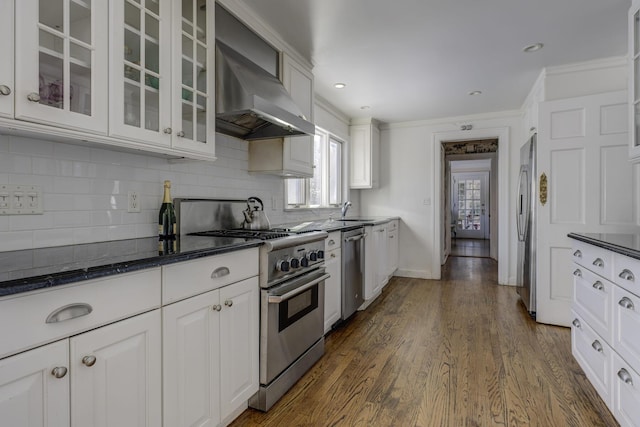 kitchen featuring tasteful backsplash, white cabinetry, stainless steel appliances, dark wood-type flooring, and wall chimney range hood