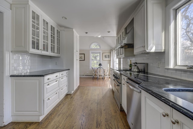 kitchen featuring wall chimney range hood, dark wood-type flooring, appliances with stainless steel finishes, dark stone countertops, and white cabinets