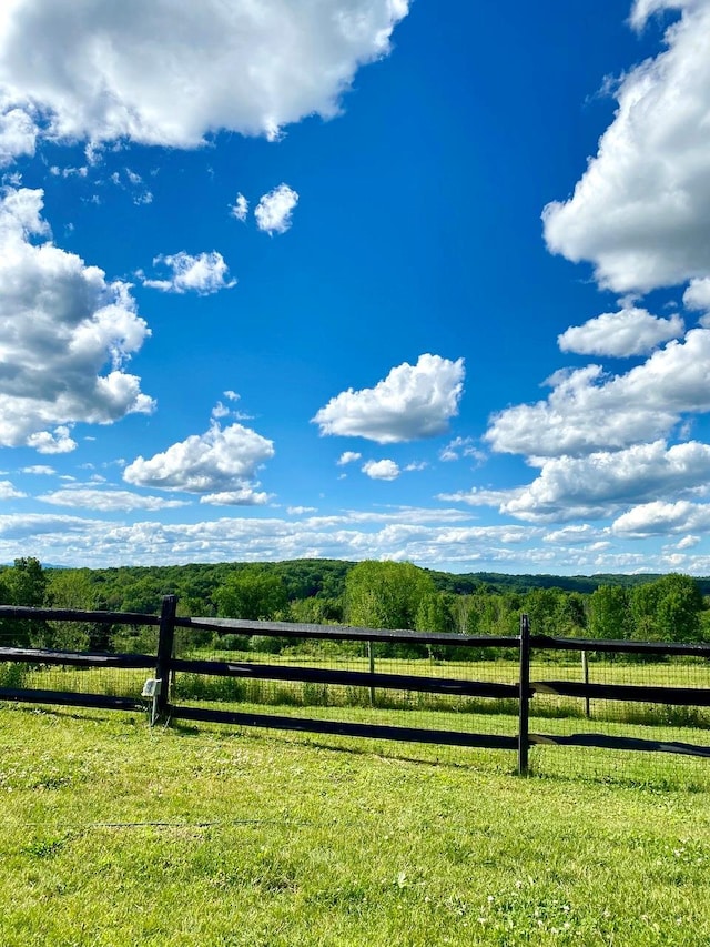 view of gate featuring a rural view, a lawn, a wooded view, and fence