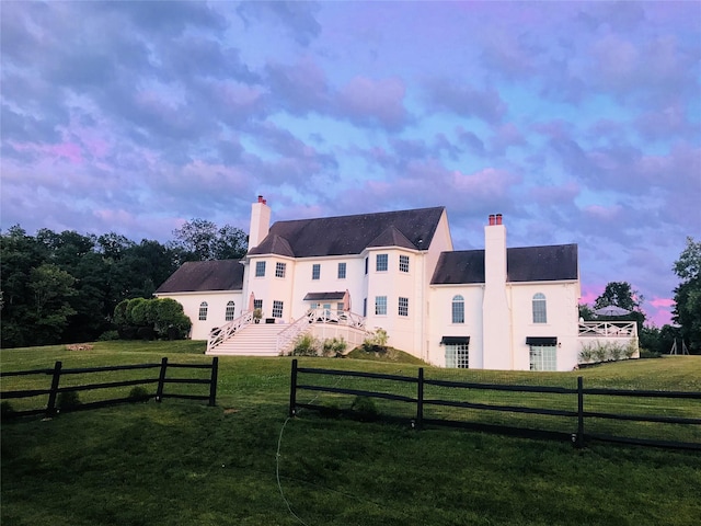 back of property at dusk featuring stucco siding, a yard, fence private yard, and a chimney