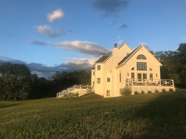 view of property exterior with stucco siding, a yard, and a chimney