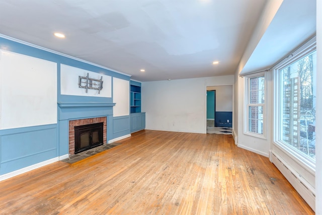 unfurnished living room with hardwood / wood-style flooring, a fireplace, built in shelves, and a baseboard heating unit