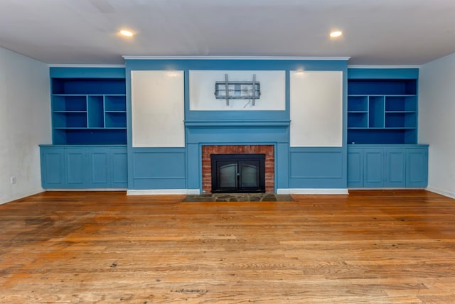 unfurnished living room with crown molding, a brick fireplace, built in shelves, and wood-type flooring