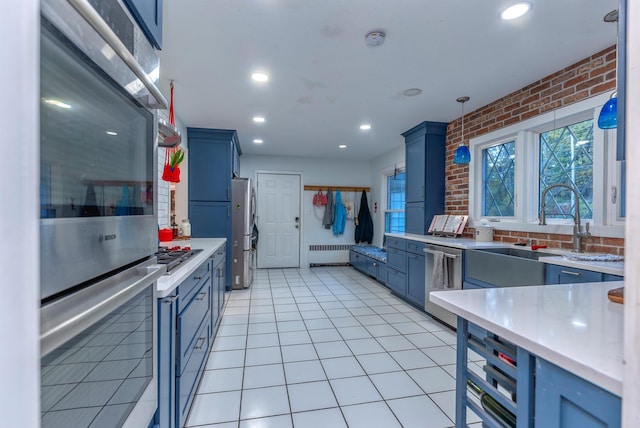 kitchen with pendant lighting, radiator, light tile patterned floors, appliances with stainless steel finishes, and brick wall