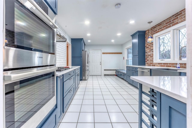 kitchen with light tile patterned flooring, brick wall, radiator heating unit, pendant lighting, and blue cabinetry