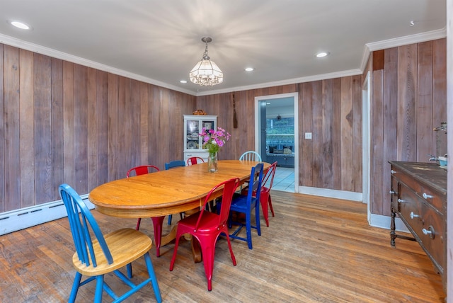 dining area featuring crown molding, wooden walls, a notable chandelier, and light hardwood / wood-style floors