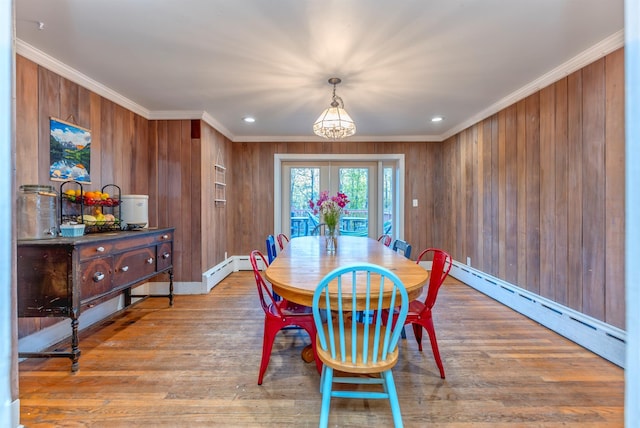 dining area featuring crown molding, a baseboard radiator, wooden walls, and light wood-type flooring