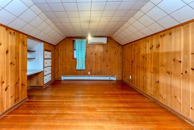 additional living space featuring vaulted ceiling, a wall mounted air conditioner, wooden walls, wood-type flooring, and baseboard heating