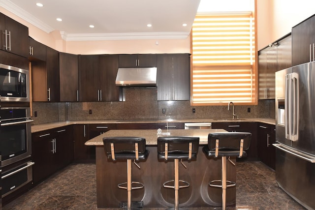 kitchen with dark brown cabinetry, a kitchen bar, a center island, appliances with stainless steel finishes, and light stone countertops