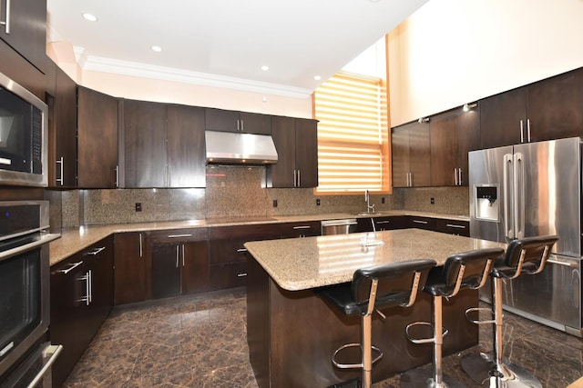 kitchen featuring a breakfast bar area, dark brown cabinets, a kitchen island, stainless steel appliances, and backsplash