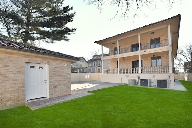 rear view of property featuring a balcony, a yard, central AC unit, and a patio area